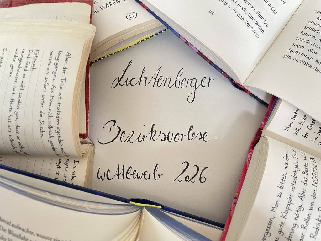Eine Fotografie des Schriftzuges "Lichtenberger Bezirksvorlesewettbewerb 2026". Die schwarze Schrift auf weißem Hintergrund ist umrandet von fünf aufgeschlagenen Büchern, von denen ein kleiner Teil der jeweiligen Seiten zu sehen ist,